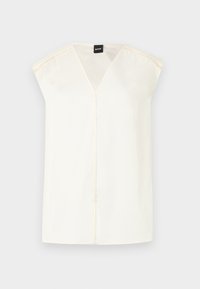 Haut sans manches couleur crème avec un col en V, texture lisse et couture délicate le long des épaules. L'étiquette de la marque est visible à l'intérieur.