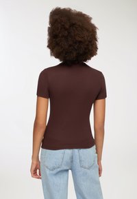 Brązowa, prążkowana bluzka z krótkim rękawem o dopasowanym kroju, zestawiona z jasnoniebieskimi, wysoko w pasie dżinsami z widocznymi tylnymi kieszeniami.