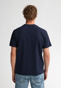 Marineblauw katoenen T-shirt met korte mouwen, ronde hals en een effen achterkant; gecombineerd met lichtblauwe spijkerbroek.