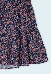 Květinové šaty s námořnickým pozadím a malými červenými a bílými květinami. Různorodý design s volánkovým lemem a štítkem na dolním okraji.