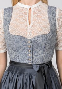 Traditionelles Kleid mit einem blauen Blumenmuster auf dem Oberteil, einer cremefarbenen Spitzenbluse und einem marineblauen Satinschleifenband, das an der Taille gebunden ist. Knopfdetails sichtbar.