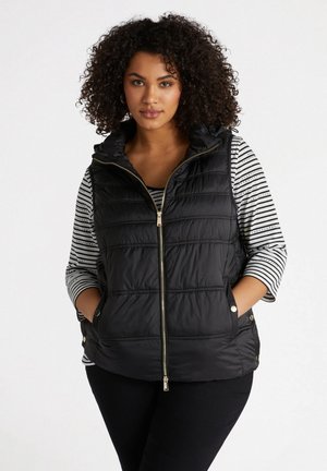 Zwarte donzen gilet met een rits aan de voorkant, capuchon en horizontaal gestikte patroon. Draag het over een zwart-wit gestreept shirt met opgerolde mouwen.