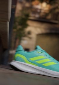 Zapatilla deportiva azul claro y amarillo neón descansando sobre una superficie plana con un fondo urbano desenfocado.