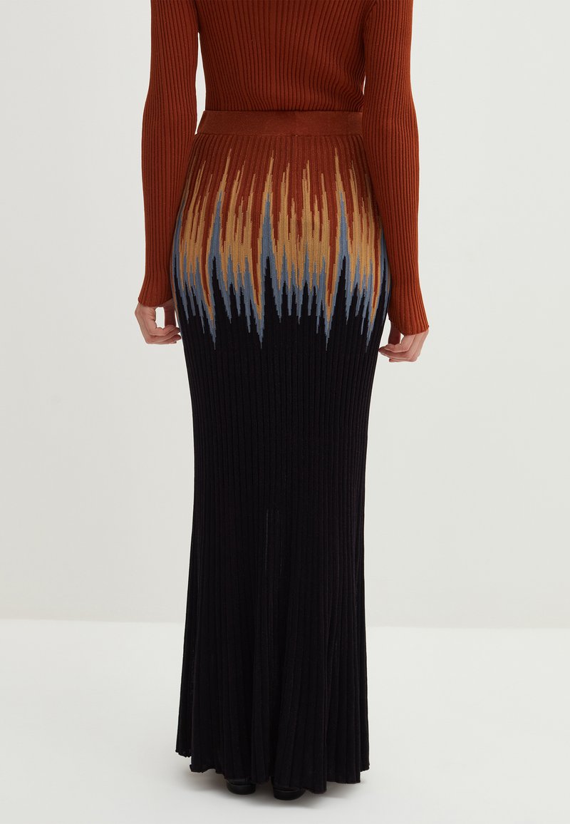 Rippendes langes Kleid mit einem schrägen, flammenartigen Muster in Brauntönen, Beige und Blau, kombiniert mit einem rostfarbenen, gerippten Langarmoberteil.