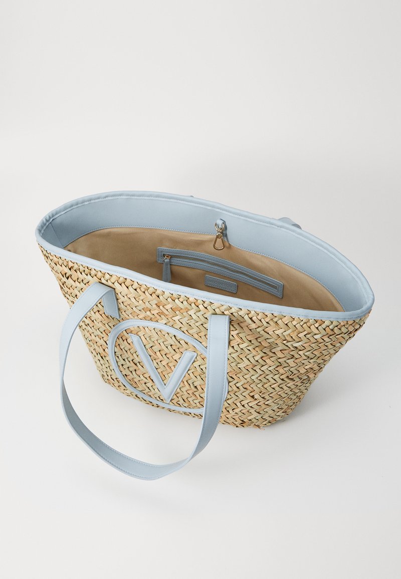 Sac de plage en paille tissée avec des bordures en cuir bleu clair, poignées rondes et un logo en forme de V. L'intérieur est doublé de tissu beige et comprend des poches.
