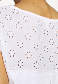 Top de algodón blanco que presenta un patrón floral bordado con detalles troquelados en la parte posterior y un escote redondeado, creando una apariencia texturizada.