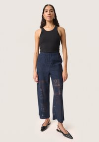 Zwarte geribbelde tanktop gecombineerd met marineblauwe cropped broek met een kanten ontwerp en een uitlopende zoom. Model draagt zwarte instappers.