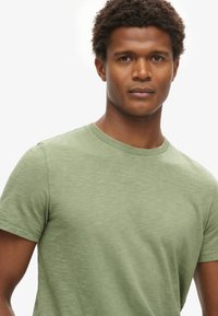 T-shirt verde chiaro a maniche corte con scollo rotondo, caratterizzato da una texture morbida e un sottile motivo melange.