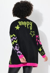 Maglione nero oversize con vivace testo verde "HAPPY", stelle, zigzag e motivi leopardati in rosa, viola e verde. Polsini e orlo a costine.