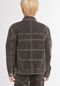 Giacca di jeans nera con colletto bottonato, dettagli di cucitura bianca e vestibilità ampia. Presenta una cucitura sul retro e tasche laterali.