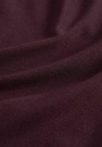 Smooth, soft fabric folds in a deep burgundy color, showing fine knit texture and gentle draping.