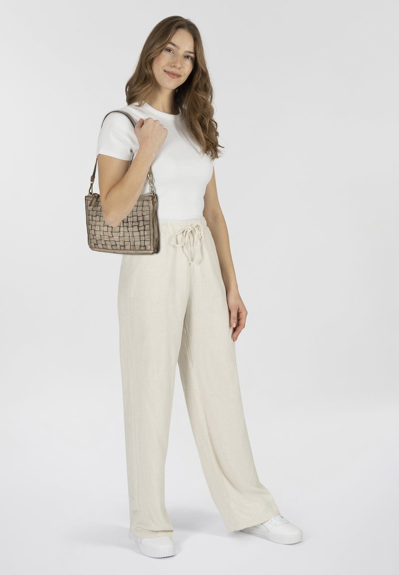 Borsa a tracolla tessuta beige con forma rettangolare, caratterizzata da una superficie testurizzata; indossata in modo informale con pantaloni larghi di colore chiaro e una maglietta aderente bianca.