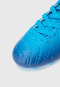 Μπλε ποδοσφαιρικό παπούτσι με λείο δέρμα στο επάνω μέρος, υφασμένα σημεία και επίπεδους κορδόνια. Το σχέδιο περιλαμβάνει στρογγυλεμένη μύτη με ραφές λεπτομέρειας.