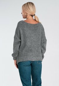 Szary sweter dzianinowy z szerokim dekoltem i opadającymi ramionami, charakteryzujący się luźnym krojem i prążkowaną strukturą. Połączony z niebieskimi dżinsami.