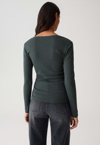 Langarmige donkergroene top met een bootlijn ontwerp, aansluitende silhouet en een gladde textuur, gecombineerd met donkergrijze spijkerbroeken met achterzakken.