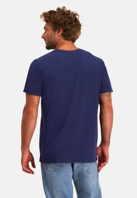 Navyblauw t-shirt met korte mouwen en een ronde hals, van zachte katoen, in een relaxte pasvorm, gedragen met lichtblauwe jeans en zichtbare tatoeages.