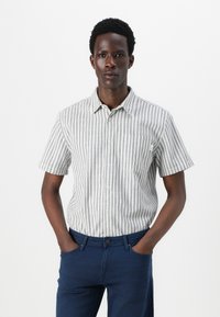 Chemise à manches courtes avec des rayures verticales bleues et blanches, avec un bouton sur le devant et une poche poitrine, fabriquée en tissu léger.