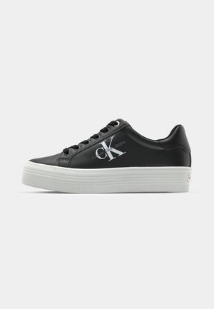 Black platform sneakers made of synthetic material with a white rubber sole. Features a logo on the side and black laces.