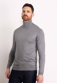 Grauer Rollkragenpullover aus weichem Strickmaterial mit figurbetontem Schnitt, gerippten Bündchen und Saum, kombiniert mit dunkelblauen Jeans.