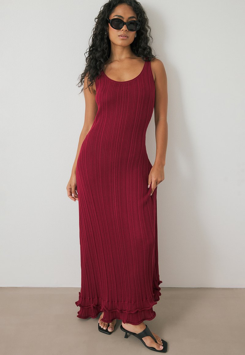 Rippent, hoch-elastisches Maxikleid in burgundy mit runden Ausschnitt, ausgestelltem Rüschensaum und glatter Textur, kombiniert mit schwarzen Sandalen und Sonnenbrille.