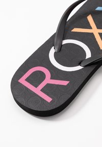 Svarte flip-flops med teksturert såle, svarte stropper og mangefargede bokstaver "ROXY" i rosa, hvitt og oransje.