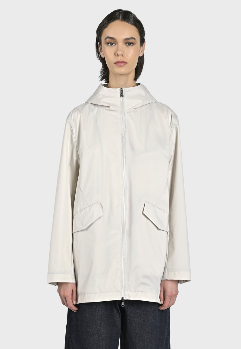 Giacca leggera color bianco sporco con cappuccio, realizzata in tessuto liscio, caratterizzata da una zip centrale e due tasche frontali con alette angolari.