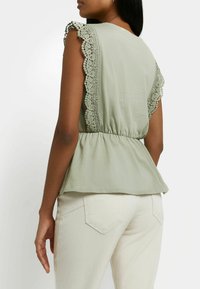 Světlý zelený peplum top s krajkovými rukávy a nařaseným pasem. Hladká látka, volný střih, kombinováno se světlými přiléhavými kalhotami.