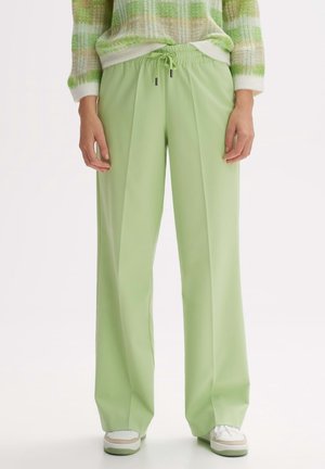 Pantalons vert clair avec une taille à cordon de serrage, présentant une coupe ample et un design plissé. Texture lisse et style minimaliste.