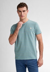 T-shirt bleu à manches courtes avec un motif de rayures dorées subtil et un col rond. Petite étiquette de logo sur la poitrine.