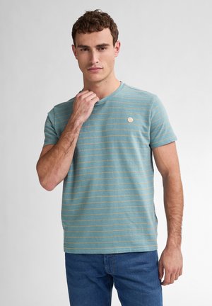 Camiseta de manga corta azul con un sutil patrón de rayas doradas y un cuello redondo. Pequeño parche de logo en el pecho.