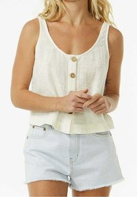 Débardeur en lin blanc avec un décolleté rond et deux boutons en bois à l'avant ; associé à un short en jean bleu clair aux bords effilochés.