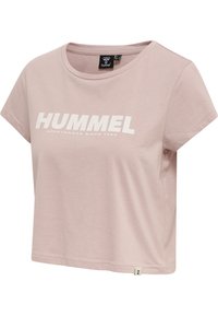 Camiseta corta de color rosa claro en tejido suave, con mangas cortas y cuello redondo, que presenta un gran texto blanco "HUMMEL" y una etiqueta con el logo en el dobladillo.