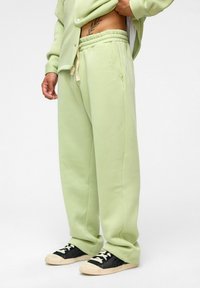 Lichtgroene joggingsbroek met een ontspannende pasvorm, elastische tailleband, aantrekkoord en zijzakken, gecombineerd met zwarte sneakers.