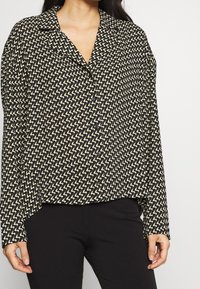 Sort og cremebluse med zigzag-mønster, lange ærmer og kraveudskæring. Fremstillet af letvægtigt stof med en afslappet pasform.