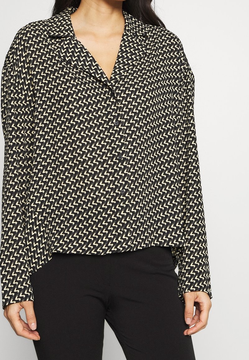 Sort og cremebluse med zigzag-mønster, lange ærmer og kraveudskæring. Fremstillet af letvægtigt stof med en afslappet pasform.
