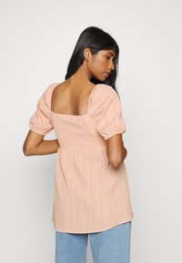 Blusa de tom pêssego, texturizada, com mangas bufantes, decote quadrado nas costas e detalhe de cintura franzida. Combinada com jeans azul claro.