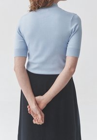 Jasnoniebieski dzianinowy top z krótkim rękawem o przylegającym kroju, gładkiej fakturze, prążkowanych mankietach i kołnierzyku z igiełkami, w połączeniu z czarną spódnicą.