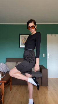 Top preto de manga longa, saia lápis castanha de cintura alta, meias brancas, tacões pretos, óculos de sol castanhos grandes, design minimalista.