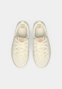 Αθλητικά παπούτσια UGG σε εκρού χρώμα, με λείο δερμάτινο πάνω μέρος, διάτρητη μύτη, καπιτονέ λεπτομέρειες και επίπεδα, κρεμ κορδόνια.