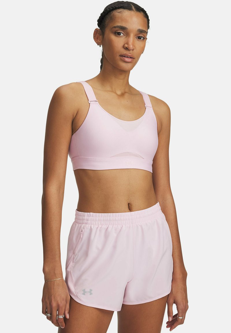 Sujetador deportivo rosa claro con tirantes ajustables y detalle de malla, combinado con pantalones cortos ligeros a juego que tienen una cinturilla elástica y un cierre lateral.