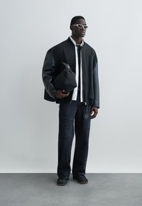 Μαύρο μπουφάν με δερμάτινα μανίκια, λευκό πουκάμισο, σκουρόχρωμο τζιν με φθαρμένες λεπτομέρειες και μαύρα παπούτσια. Αξεσουάρ: μαύρη τσάντα.