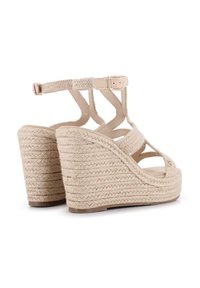 Sandalias de cuña beige con material de yute trenzado, punta abierta, múltiples correas y hebilla ajustable en el tobillo. Suela texturizada notable.