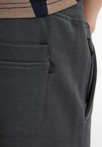 Mörkgrå sweatpants med en texturerad yta, som har en bakficka, ribbat midjeband och en liten märkesetikett på fickan.