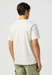 Short-sleeved, light beige t-shirt with a crew neck, made of soft cotton fabric. Features a smooth texture, without decorative elements.
