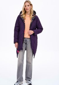 Fialová prošívaná péřová bunda s květinovým vzorem uvnitř, která má kapuci a růžovou akcentovou visačku. Spárováno se šedými džíny a teniskami.