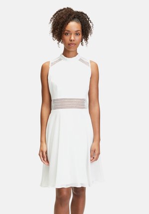 Robe blanche avec un corsage ajusté, des accents de panneaux en dentelle aux épaules et une jupe évasée. Tissu doux avec un léger éclat.