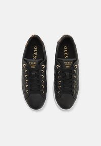 Svarta syntetiska sneakers med gyllene ögla, med ett strukturerat mönster på sidan och vita gummisulor. Märkeslogotyp på tungan.