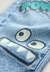 Tkanina dżinsowa w jasnoniebieskim kolorze z graficznym wzorem dużych oczu i zębów. Tekstura jest prążkowana z wyglądem przypominającym kreskówkę.