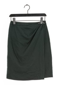 Tmavě zelená zavinovací sukně vystavená na černém ramínku. Materiál vypadá měkký s jemnou strukturou; má zkroucený detail na jedné straně.