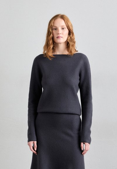 Pull en tricot gris foncé, ajusté, avec un large col et des manches longues, associé à une jupe moulante assortie, toutes deux en tissu texturé.